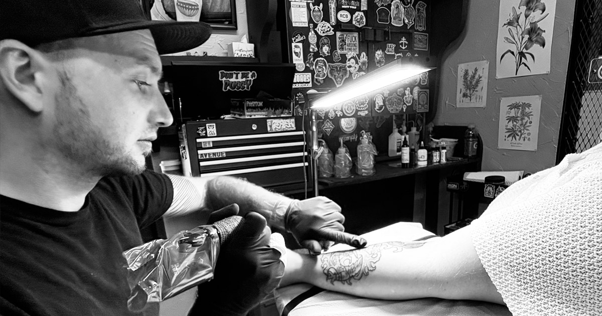Travis at the shop tattooing a client.
