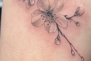 Minimalist tattoo features a delicate black and white depiction of a cherry blossom branch on the upper shoulder.