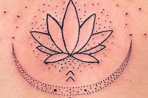 The tattoo features a central lotus flower design surrounded by dots and symbols, extending vertically down the spine.
