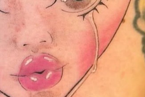 The tattoo depicts a stylized, crying face within a heart-shaped outline.