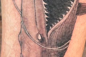 The tattoo depicts a monstrous whale dragging a struggling deer, symbolizing the destructive power of nature .